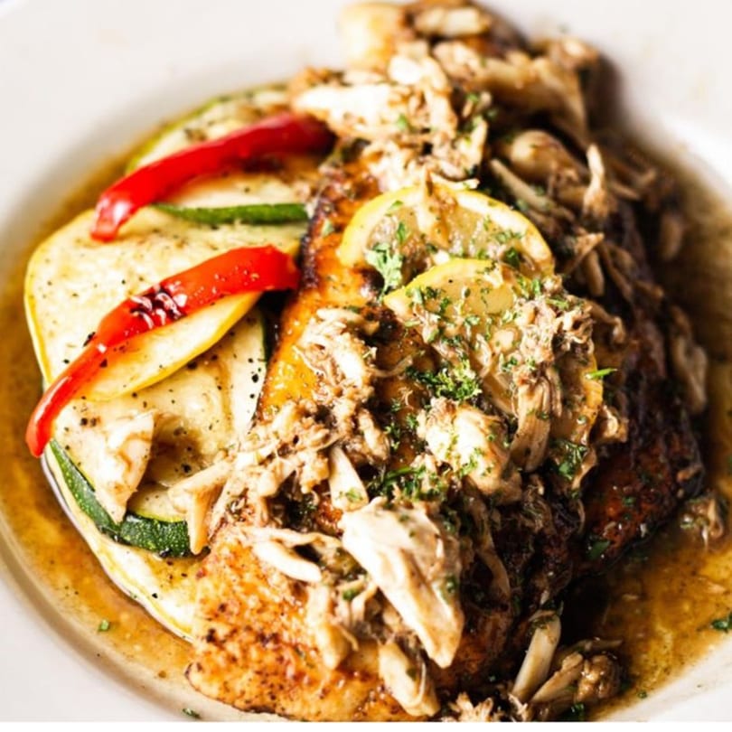 Pujo St Cafe's American dish with grilled fish, crab meat, lemon slices, and roasted vegetables.