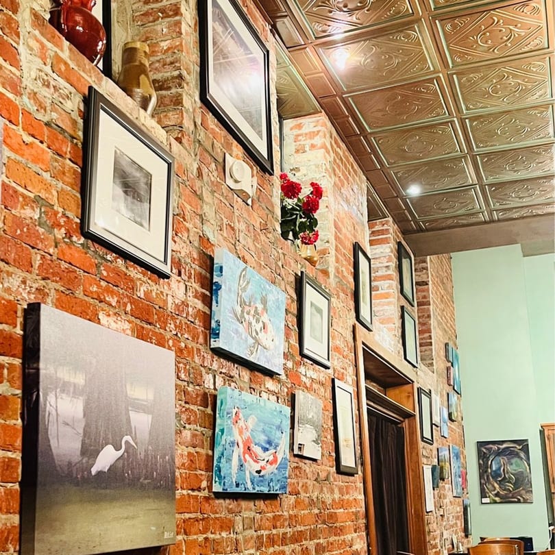 A brick wall adorned with various framed pictures and paintings, with a decorative ceiling.