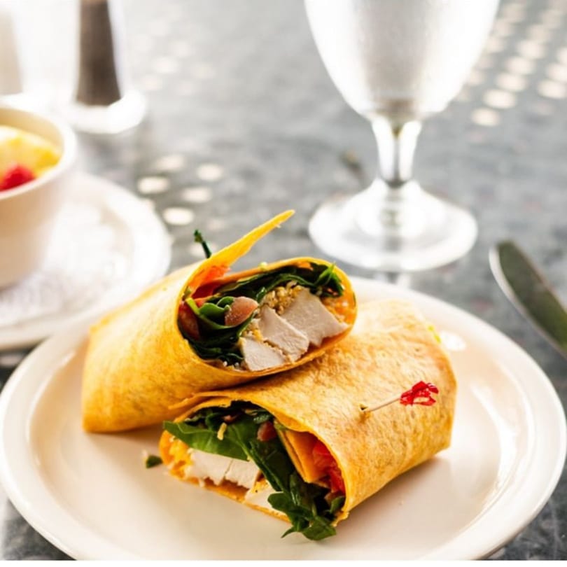 Two halves of a chicken and spinach wrap on a white plate at Pujo St Cafe.
