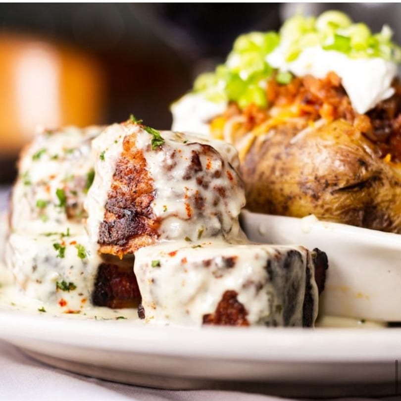 Pujo St Cafe's American cuisine features steak bites with creamy sauce and a loaded baked potato.